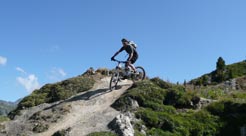 A mountain biker navigating a rocky trail against a clear blue sky.